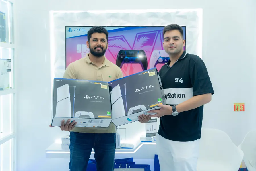 Two customers holding PS5 Digital Edition boxes in front of the in-store display